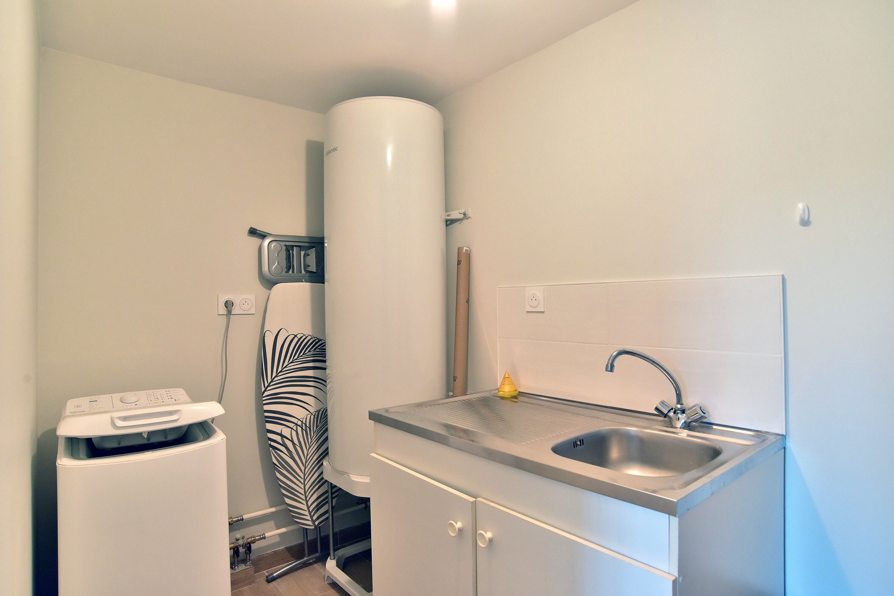 Una cocina compacta con un lavamanos integrado, una pequeña encimera y una lavadora blanca.