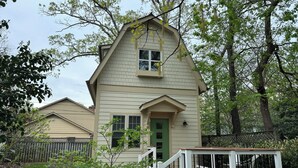 A two-story house with a green door, a small porch with white railings, and a garden area with a table and chairs.