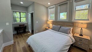 A bedroom with a bed, two bedside tables, a desk, a chair, and a ceiling fan.