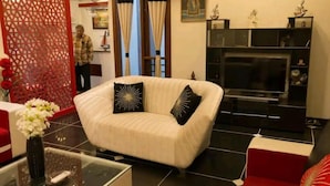 A living room with a white sofa, black cushions, a glass coffee table, and a TV stand. - The place is very much pleasing , adorable and comfortable . Also amazing decor  (Delhi)