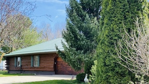A log cabin with a green roof, surrounded by lush greenery and tall trees. - Log Cabin Haus, Amish Country. 
Shipshewana, Indiana near Pumpkinvine Trail (Shipshewana)