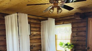 A wooden cabin bedroom with a large bed, a ceiling fan, a window with curtains, a bathtub, and a potted plant. - Log Cabin Haus, Amish Country. 
Shipshewana, Indiana near Pumpkinvine Trail (Shipshewana)