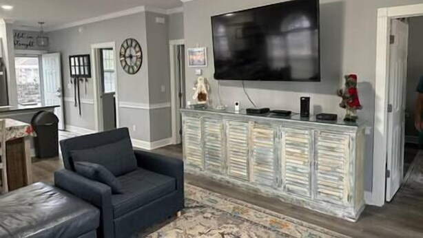 A living room with a large flat-screen TV mounted on the wall, a dark-colored sofa, and a glass-fronted cabinet with decorative items. - Beautiful Condo on Golf Course (Horry County)