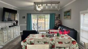 A dining area with a table set for four, a sofa, a television, and a window with curtains. - Beautiful Condo on Golf Course (Horry County)