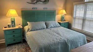 A bedroom with a bed, two nightstands, a wall-mounted lamp, and a window with blinds. - Beautiful Condo on Golf Course (Horry County)
