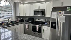 A kitchen with white cabinets, a stainless steel refrigerator, a microwave, a coffee maker, and an oven. - Beautiful Condo on Golf Course (Horry County)