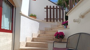 A set of beige stone stairs leading up to a white wall with a wooden fence. There are potted plants on the wall and a metal chair with a cushion at the bottom of the stairs. - Marleneee! (Torre a Mare)