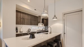 Une cuisine moderne dotée d’un grand îlot central, de meubles en bois foncé, d’appareils électroménagers en acier inoxydable et de luminaires suspendus.