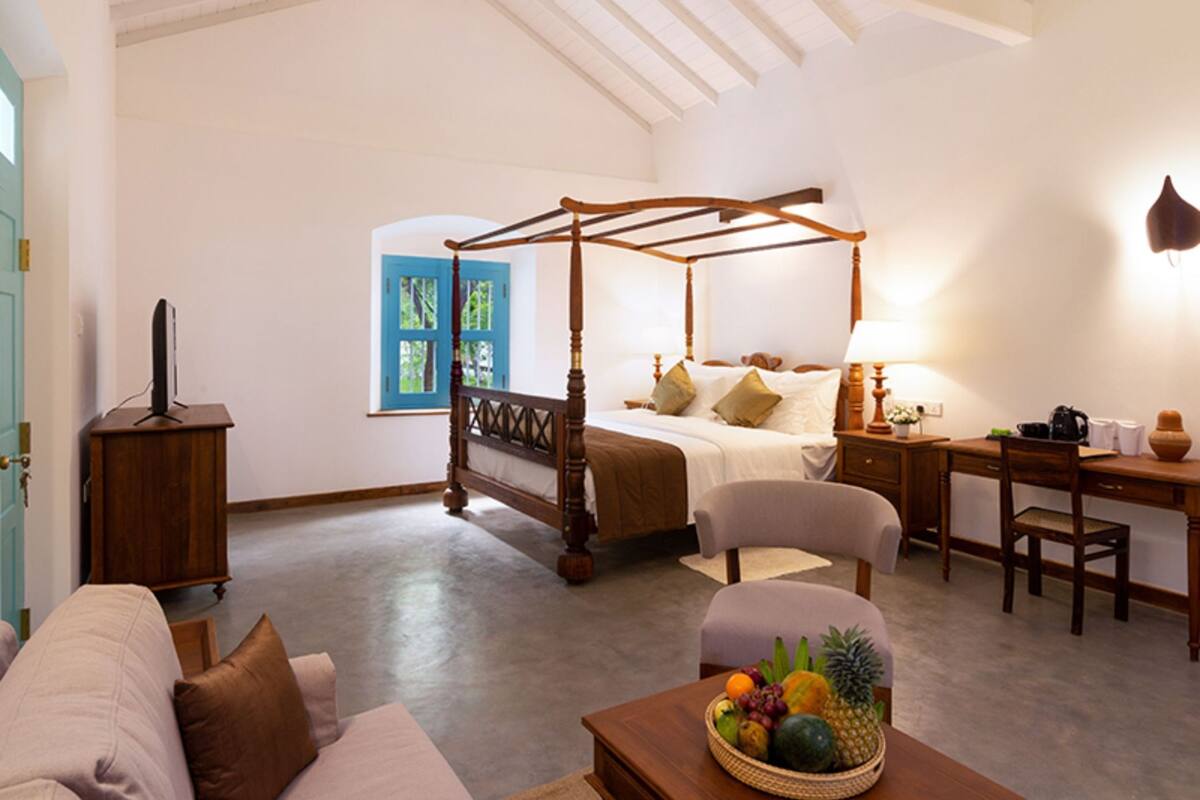 Een slaapkamer met een hemelbed, een bureau, een stoel en een mand met fruit.