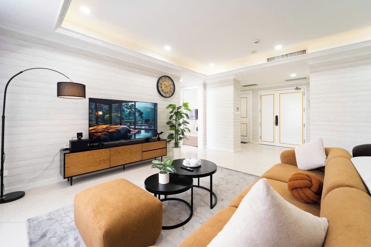 A modern living room with a flat-screen TV, sofa, coffee table, and a potted plant.