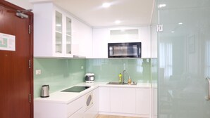 A compact kitchen with white cabinets, a microwave, a kettle, and a sink. - Spacious 2BR Lancaster (Ho Chi Minh City)