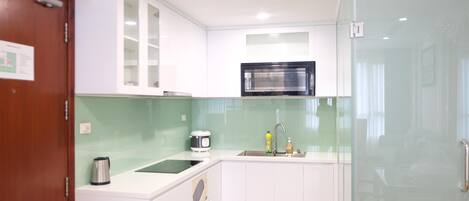 A compact kitchen with white cabinets, a microwave, a kettle, and a sink.