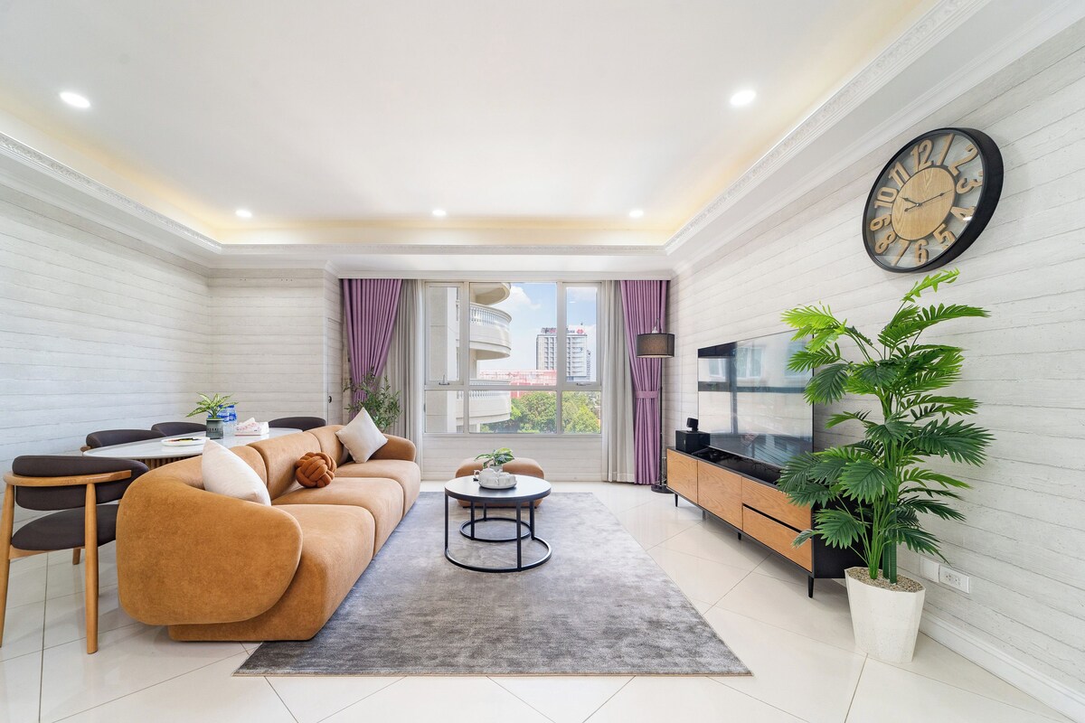A modern living room with a sofa, coffee table, TV, and a large window with curtains.