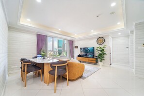 Una sala de estar moderna con comedor, un sofá, un televisor y un ventanal con cortinas.