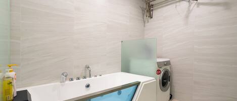 A modern bathroom with a bathtub, a washing machine, and a glass shower enclosure.