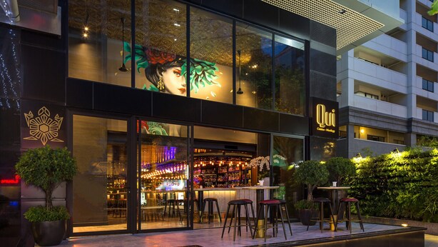 A modern bar with a glass facade, outdoor seating, and a decorative mural. - Spacious 2BR Lancaster (Ho Chi Minh City)