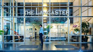 The entrance of The Langaster hotel with a modern glass facade, a security guard at the entrance, and potted plants inside. - Spacious 2BR Lancaster (Ho Chi Minh City)
