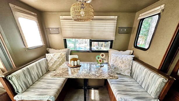 Ein gemütliches Wohnmobil-Interieur mit einem zentralen Tisch, gepolsterten Sitzgelegenheiten und Fenstern mit Blick ins Freie.