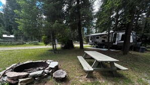 Ein Campingplatz mit Picknicktisch und Feuerstelle, umgeben von Bäumen.