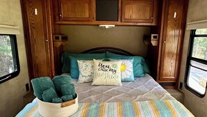 Ein gemütliches Schlafzimmer in einem Wohnmobil mit einem Bett, Kissen, einer Decke und einem Wäschekorb voller Handtücher.