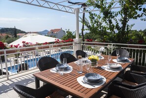 Une table en bois, dressée pour le repas, entourée de chaises, avec une piscine en arrière-plan et une pergola blanche ornée de fleurs.