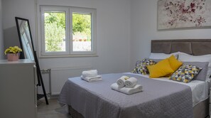 Un lit bien fait, avec des oreillers, un radiateur, une fenêtre donnant sur un paysage verdoyant et un tableau accroché au mur.