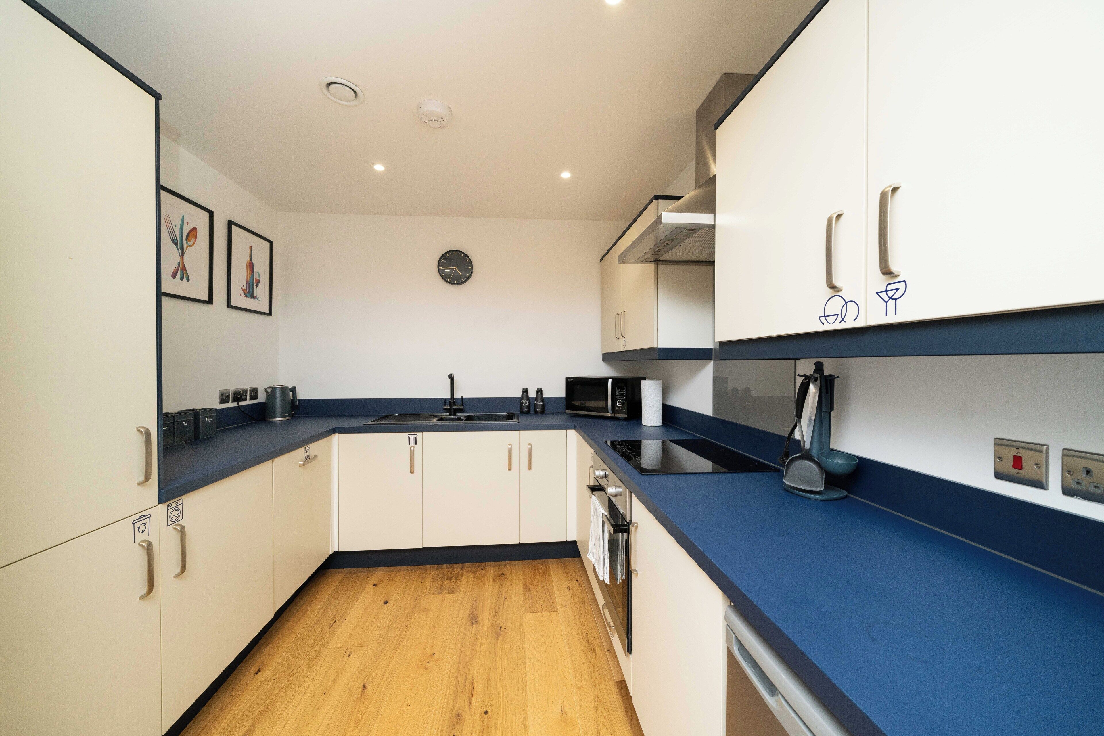 A modern kitchen with white cabinets, a blue countertop, a microwave, a sink, and a clock on the wall.