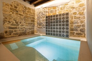 Piscina interna con pareti in pietra e un elemento d'acqua azzurro cristallino.