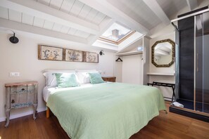 Una camera da letto con un lucernario, un letto con copripiumino verde, un comodino in legno, un armadio e uno specchio a parete.