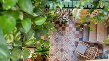 Un patio empedrado con un diseño a cuadros, una silla de mimbre y plantas en macetas.