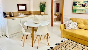 A modern kitchen with white cabinets, a dining table with chairs, a yellow sofa, and a painting on the wall. - JOLLI One-Bedroom Apartment (Rovinj)