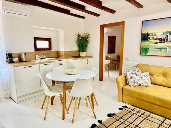 Une cuisine moderne avec des meubles blancs, une table à manger avec des chaises, un canapé jaune et un tableau accroché au mur.