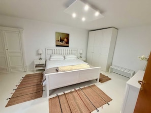 Un dormitorio con cama, mesitas de noche, un armario y un cuadro en la pared.