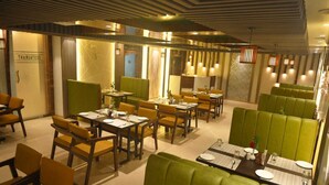 A restaurant with green booths and yellow chairs, wooden tables, and a modern ceiling design. - Hotel Jatashankar Palace (Chhatarpur)