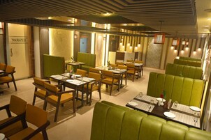 A restaurant with green booths and yellow chairs, wooden tables, and a modern ceiling design.