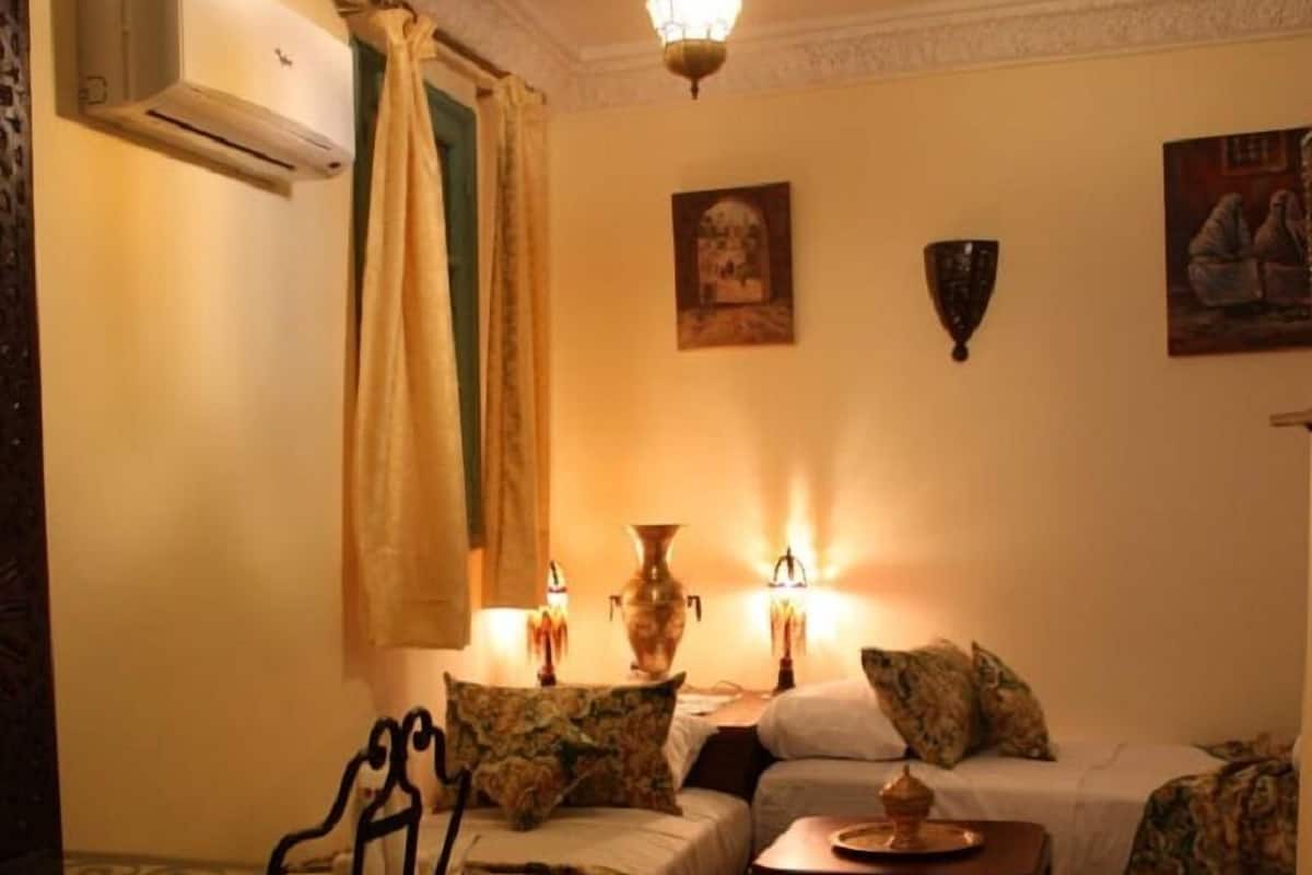 A cozy room with two beds, a red carpet, a table with a vase, and a hanging light fixture.