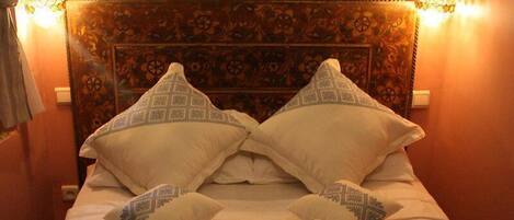 A bed with a decorative headboard, two wall-mounted lamps, and a swan-shaped towel arrangement.