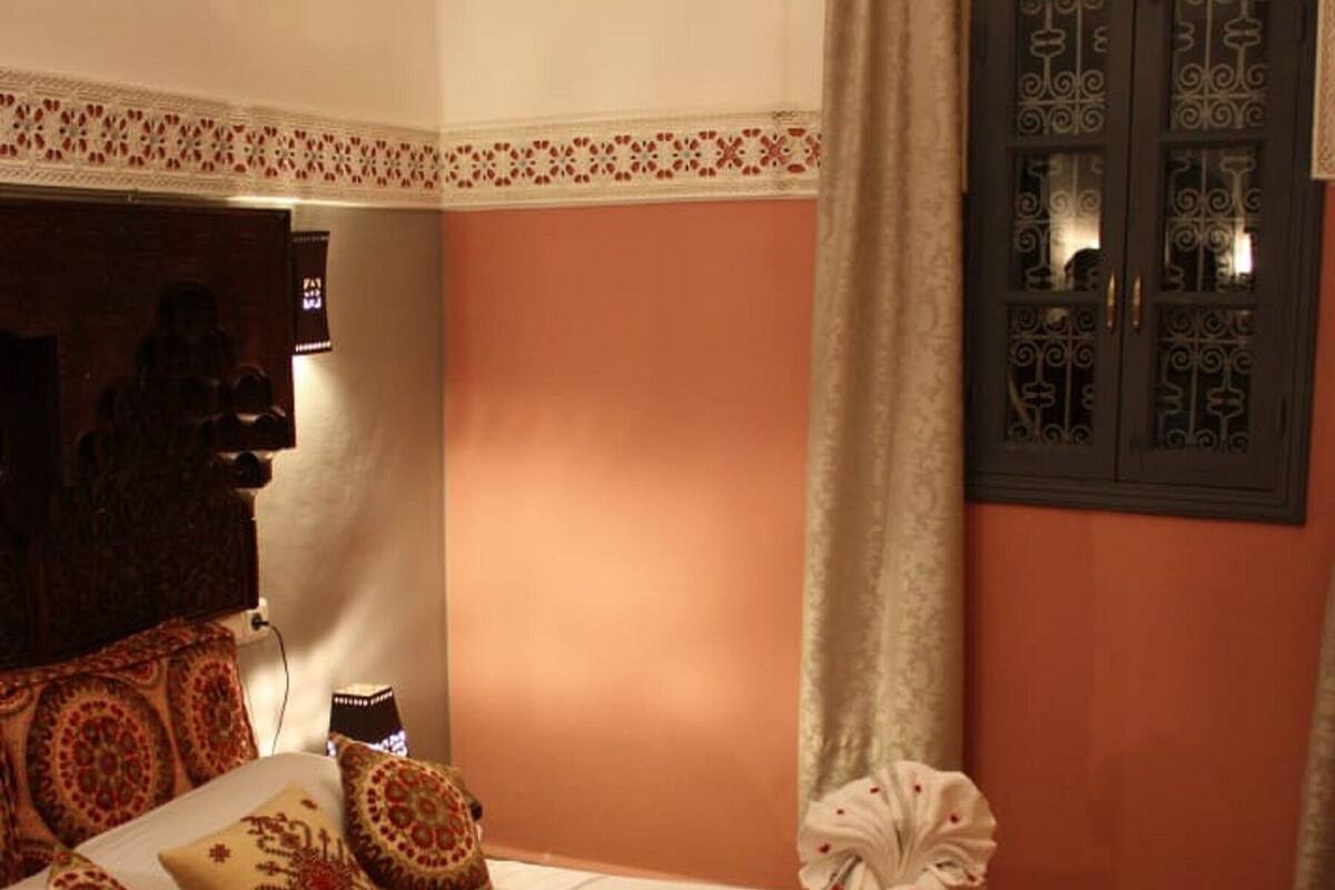 A neatly made bed with patterned pillows and a decorative towel, a wall-mounted air conditioner, and a door with intricate designs.