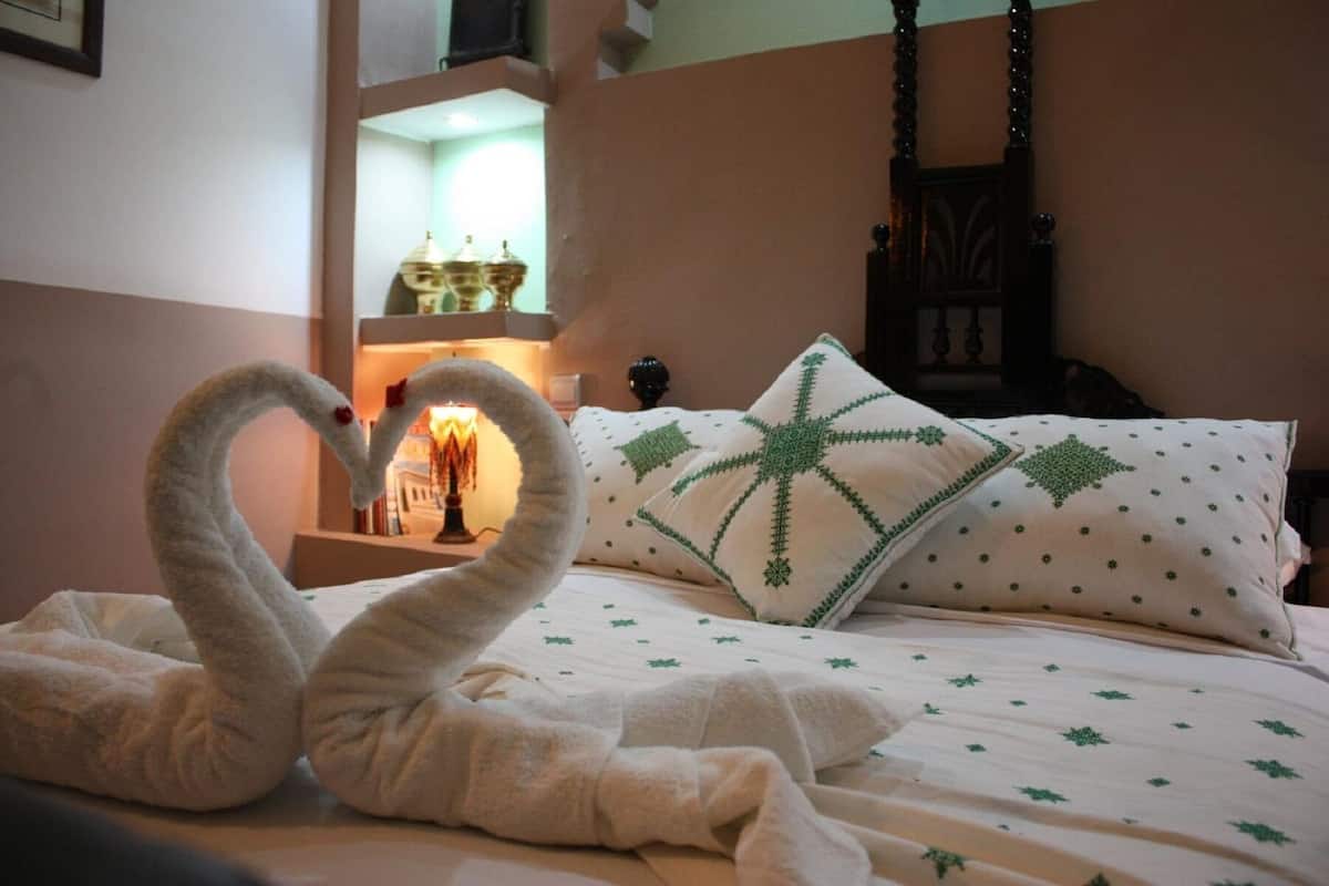 A bed with a white and green patterned bedspread, a pillow with a green geometric design, and two swan-shaped towels on the bed.