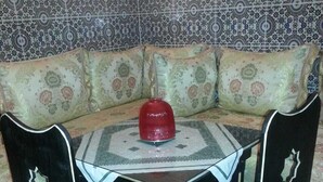 A corner seating area with a patterned sofa, a small table with a red object, and two chairs with green cushions. - Ryad Dar al Maknassia (Meknes)