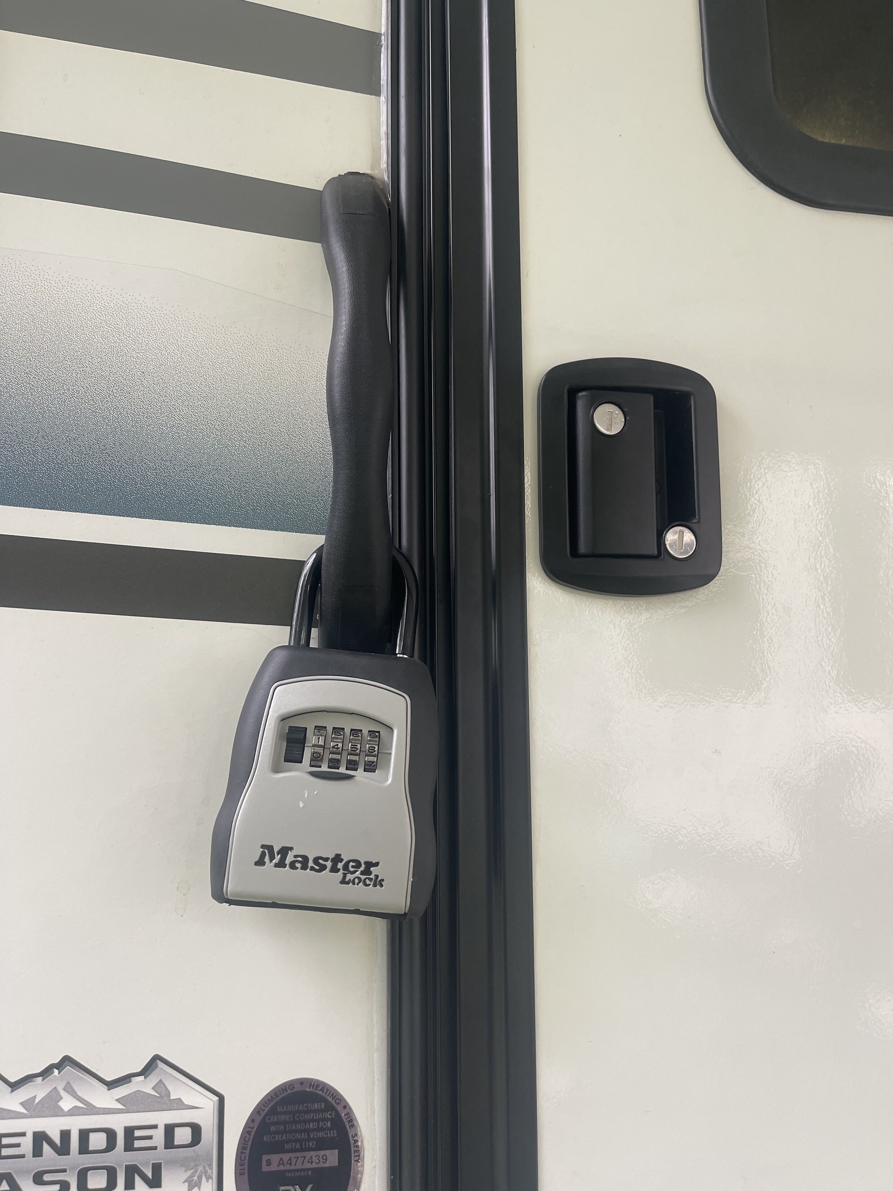 Eine Tür mit einem Master Lock Vorhängeschloss, einem Schlüsselloch und einem kleinen rechteckigen Gegenstand daneben.