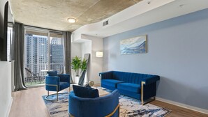 A modern living room with a blue sofa, matching armchairs, and a large window with a city view. - Royal Retreat (Atlanta)
