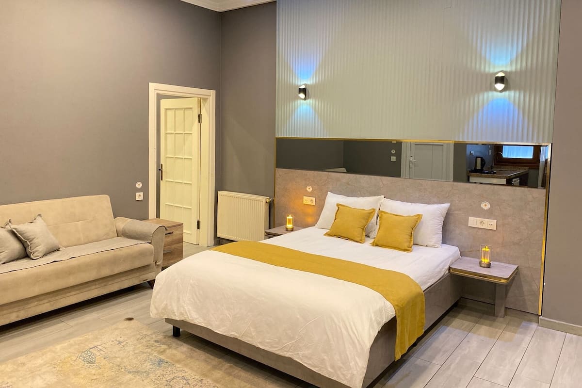 A bedroom with a bed, a bedside table, a nightstand, a mirror, a radiator, and a door.