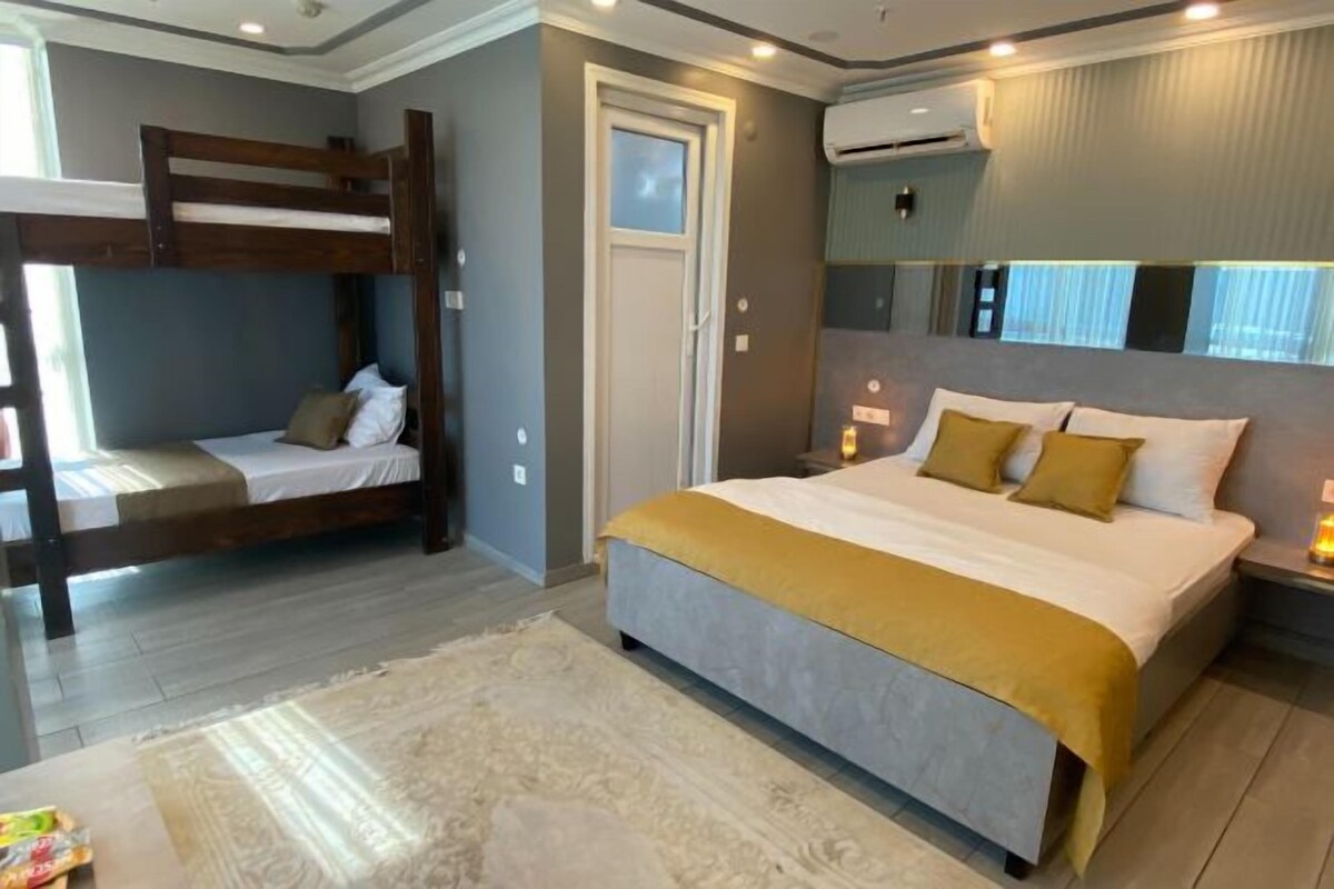 A bedroom with a bunk bed, a large bed, a door, and an air conditioning unit.