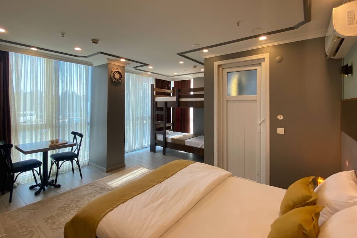 A hotel room with a large bed, a desk with a chair, a bunk bed, and a window with curtains.