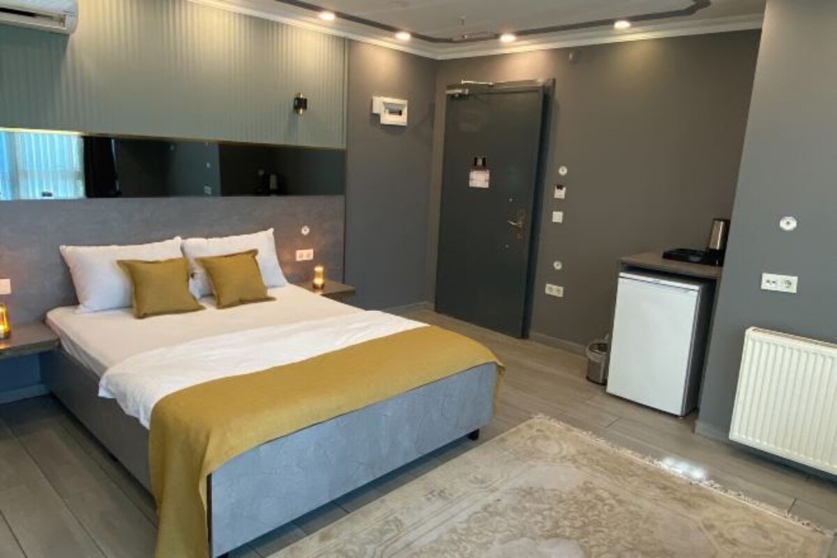 A modern bedroom with a bed, bedside tables, a small white refrigerator, and a door.