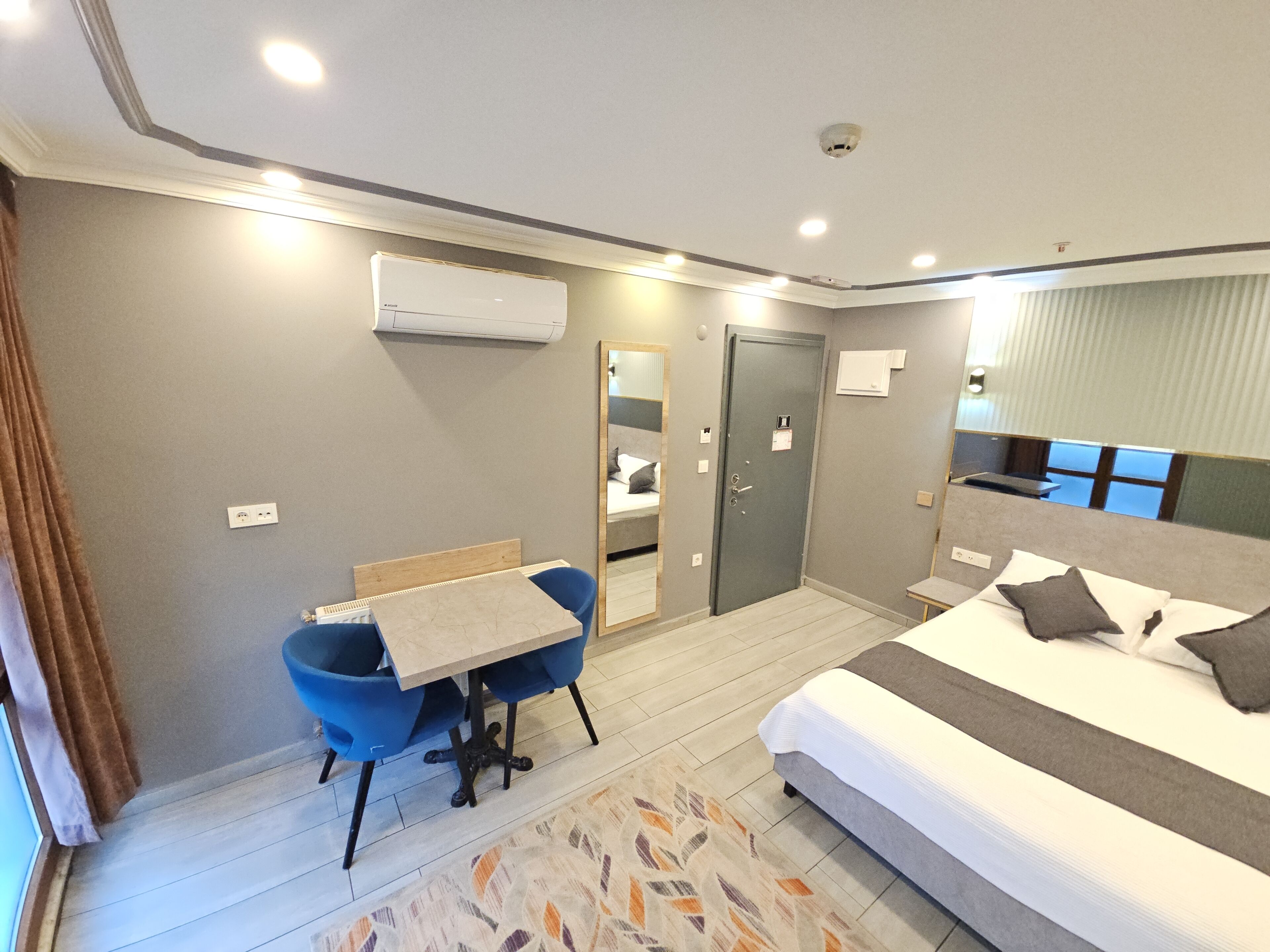 Une chambre d’hôtel comprenant un lit, un bureau avec une chaise, un appareil de climatisation, un miroir et une porte.