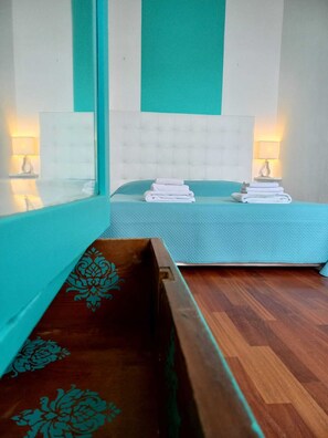 Ein Hotelzimmer mit zwei Betten, jeweils mit blauer Bettdecke und weißen Kissen. Zwei Nachttischlampen, eine Holzbank mit floralen Schnitzereien und ein Holzboden sind ebenfalls vorhanden.