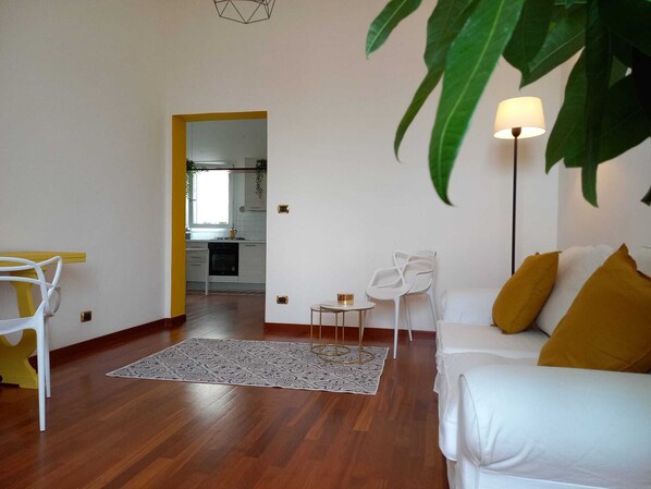 A modern living room with a white sofa, a yellow accent wall, and a large green plant.