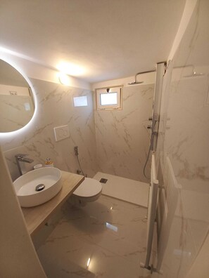 Ein modernes Badezimmer mit rundem Spiegel, Waschbecken, Toilette und Dusche.